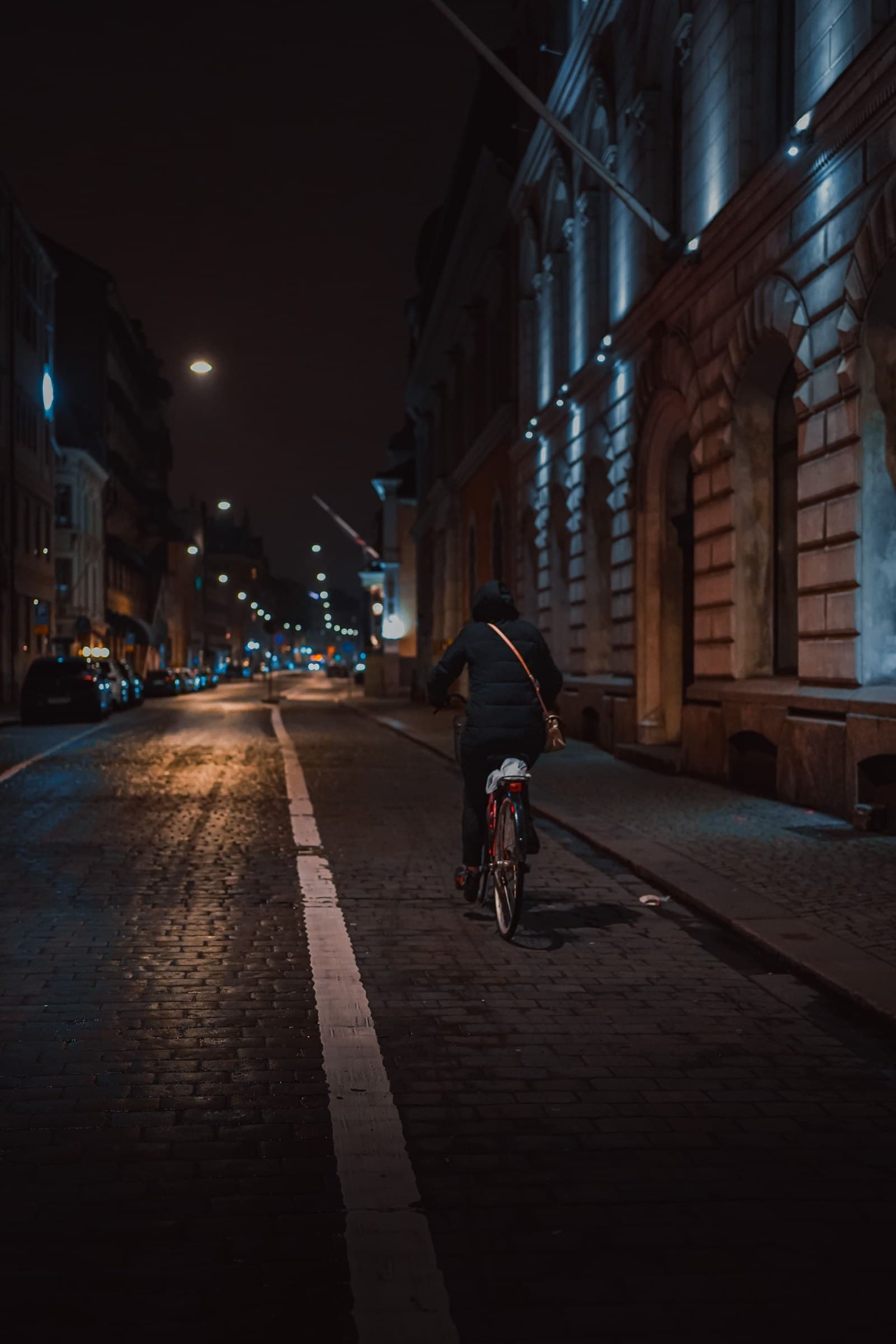 Ciclista de costas em uma rua de paralelepípedos à noite, sob a luz dos postes